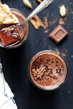 two glasses filled with chocolate desserts on top of a black table next to pieces of bread