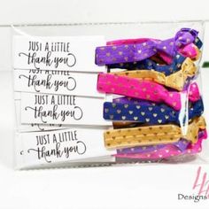 several small hair clips in a clear box with thank you notes on them and pink, purple, blue, and gold polka dots