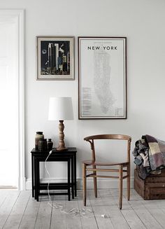 a chair and table in a room with pictures on the wall above it, next to a lamp