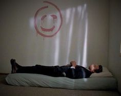 a man laying on top of a bed in front of a wall with a smiley face drawn on it