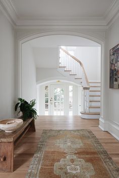 an entryway with stairs and a rug on the floor next to a wooden bench