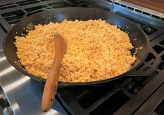 a frying pan filled with food on top of an open stove burner next to a wooden spatula