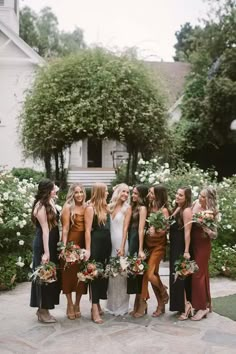 a group of women standing next to each other in front of some bushes and flowers