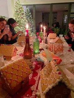 a group of people sitting around a table with gingerbread houses and candles on it