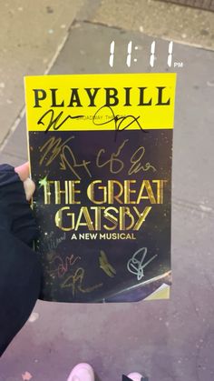 someone holding up a copy of playbill's the great gatsby book