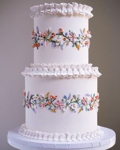 a three tiered white cake with colorful flowers on the top and bottom, sitting on a pedestal