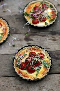 three small tarts with tomatoes and sprouts on them sitting on a wooden table