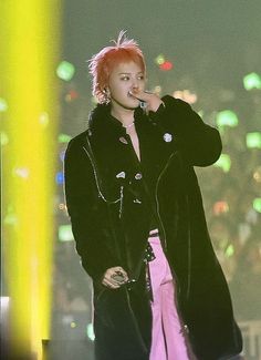 a woman with pink hair and black coat on stage