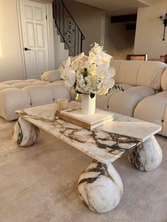 a marble coffee table with white flowers in a vase on top of it next to couches