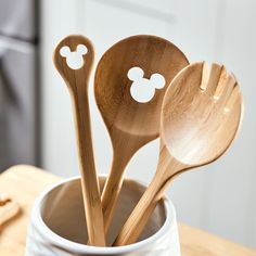 wooden spoons with mickey mouse faces are in a white cup on a table next to utensils