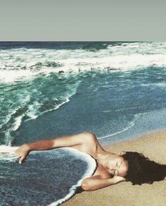 a woman laying on top of a sandy beach next to the ocean with waves coming in