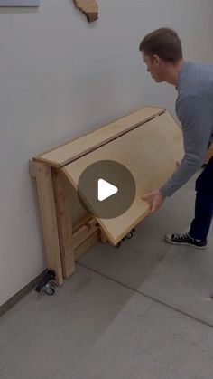 a man standing in front of a wooden table with wheels on the floor and one hand reaching for it