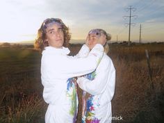 a man holding a baby in his arms while standing next to a field at sunset