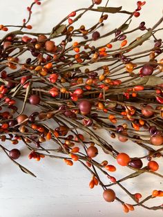 some branches with red berries on them sitting on a white table next to an orange vase