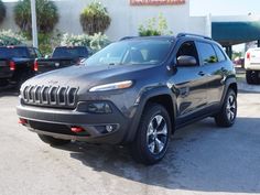 a gray jeep is parked in front of a dealership with other cars behind it