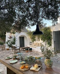 an outdoor table with plates and food on it in front of a whitewashed house