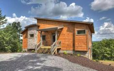 a small wooden cabin sitting on top of a gravel lot next to trees and bushes