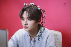 a young man with flowers in his hair sitting at a desk looking off to the side