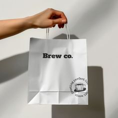 a person's hand holding a paper bag that says brew co