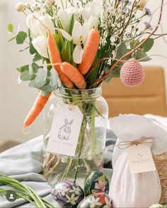 a vase filled with carrots and flowers next to an easter egg on a table