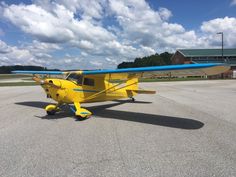 a small yellow airplane sitting on top of an airport tarmac with clouds in the background