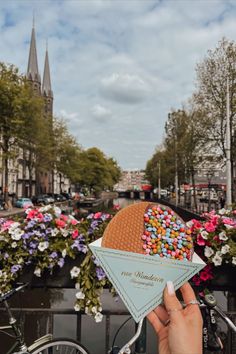 a person holding an ice cream cone with sprinkles in front of flowers