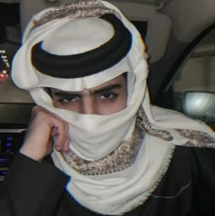 a man wearing a headscarf sitting in the back seat of a car with his hand on his face