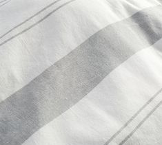 a white and grey blanket laying on top of a bed next to a pillow case