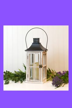 a white lantern sitting on top of a table next to purple flowers and greenery