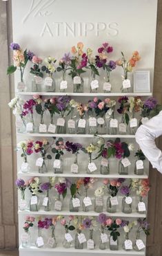 the wall is filled with flowers and small tags on each shelf, which are labeled with names