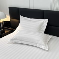 a bed with white sheets and pillows on top of it next to a night stand