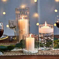 three candles sitting on top of a table next to wine glasses