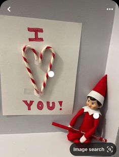 an elf is hanging on the wall next to a paper heart and candy canes