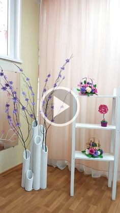 two white vases filled with purple flowers on top of a wooden floor next to a window