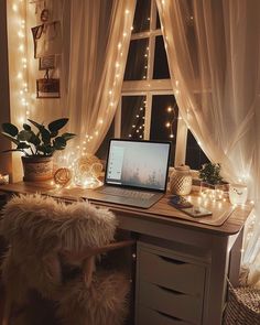 a laptop computer sitting on top of a desk next to a window covered in fairy lights