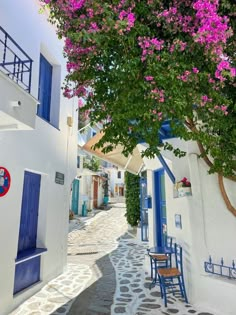 an alleyway with blue and white buildings and purple flowers on the tree in front