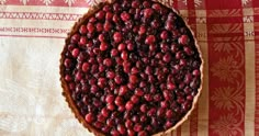 a pie with cranberries on top sitting on a red and white table cloth