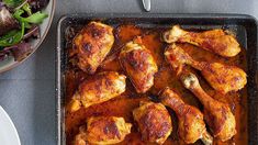 a pan filled with chicken legs covered in gravy next to a bowl of salad