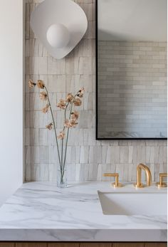 a vase with flowers sitting on top of a bathroom counter next to a mirror and sink