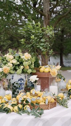 lemons and flowers are on display in vases at an outdoor table with white cloth