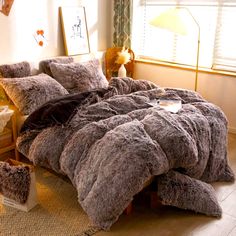 a bedroom with a bed covered in grey fluffy blankets and pillows, next to a window