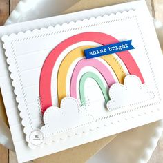 a close up of a card with a rainbow and clouds on the front, along with a white plate