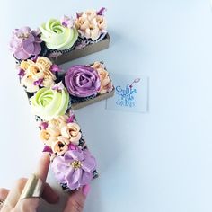 a person holding a cupcake in the shape of the letter f with flowers on it