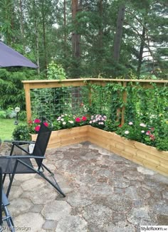 a table and chairs on a patio with an umbrella in the back ground, surrounded by flowers