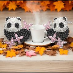 two panda bears sitting next to each other near a cup and saucer on leaves