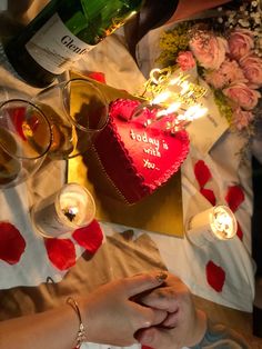 two people sitting at a table with wine and candles in the shape of a heart