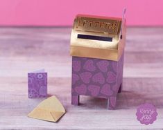 a small purple box with gold lettering on it next to some paper hearts and a yellow envelope