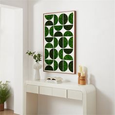 a white console table topped with a vase filled with flowers and greenery next to a painting on the wall