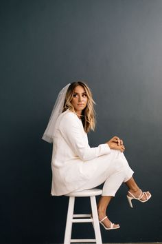 a woman sitting on top of a white stool wearing a wedding dress and veil over her head