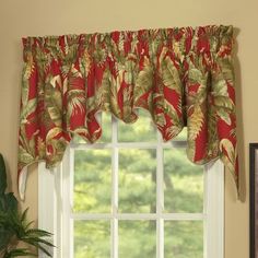 a window with a red and green curtain hanging from it's side next to a potted plant